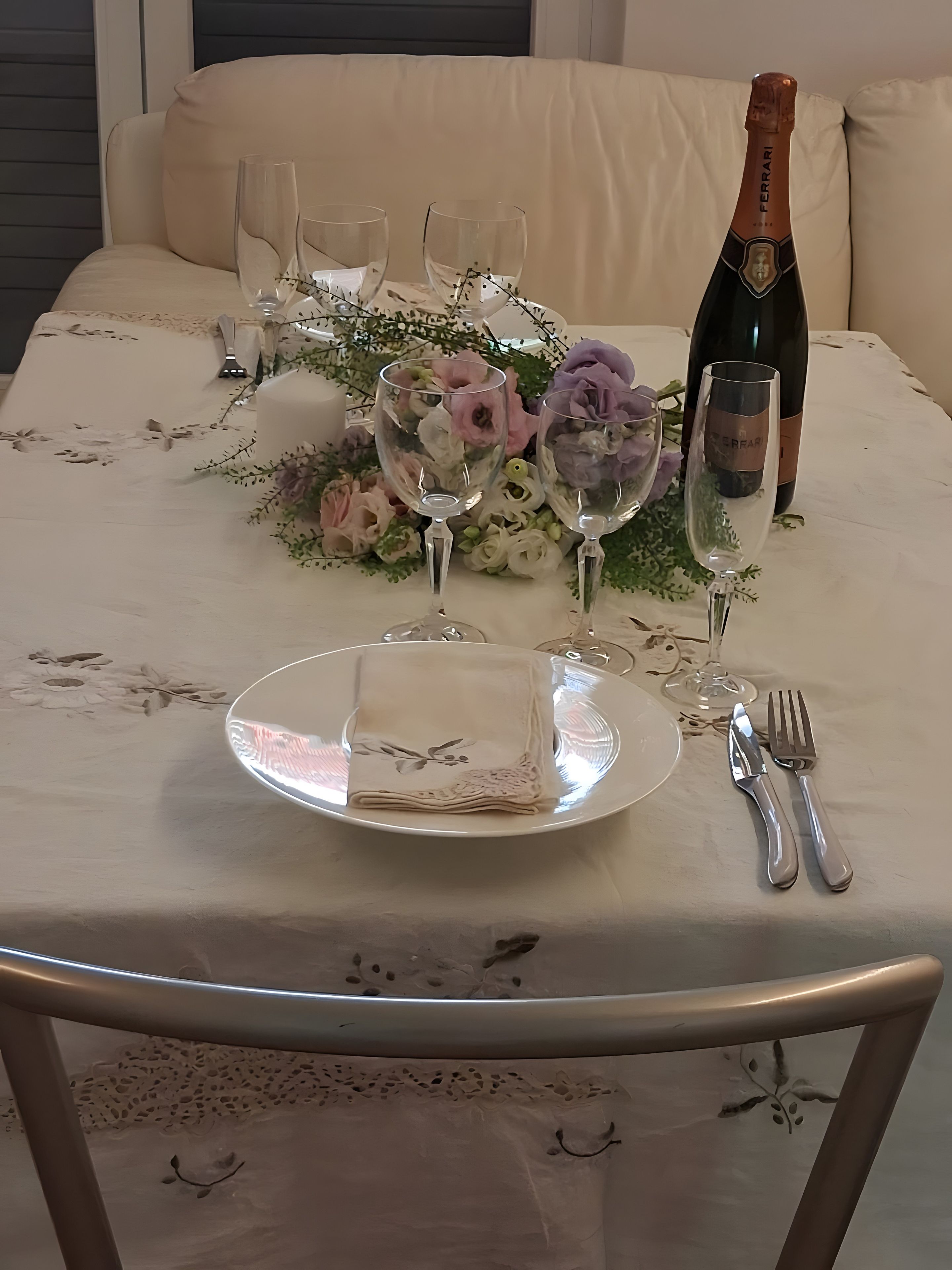 Une table dressée avec une serviette pliée, deux verres à vin, une bouteille de champagne et des couverts.