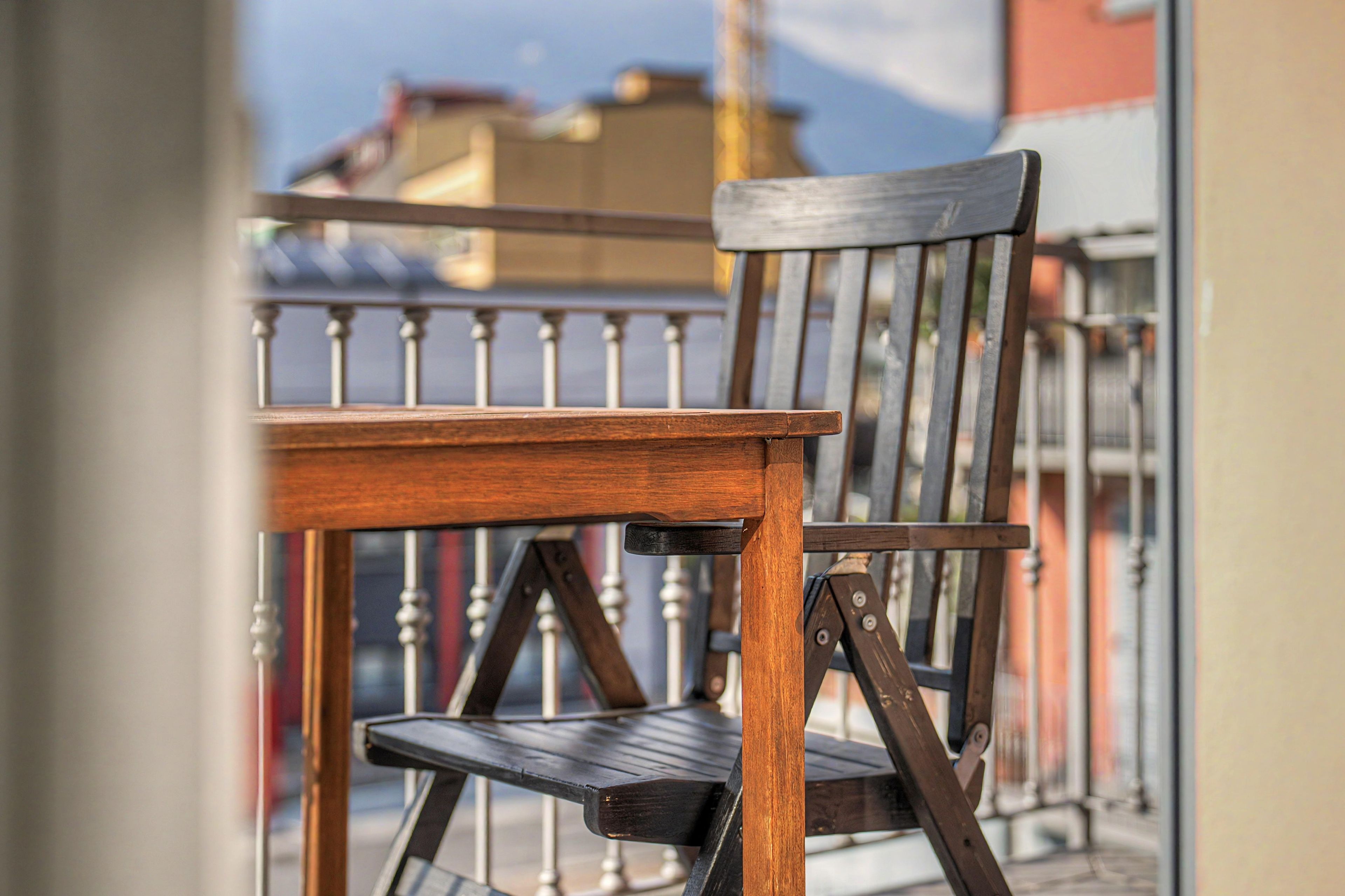 Una sedia di legno con struttura metallica, posizionata su un balcone dotato di ringhiera in metallo.