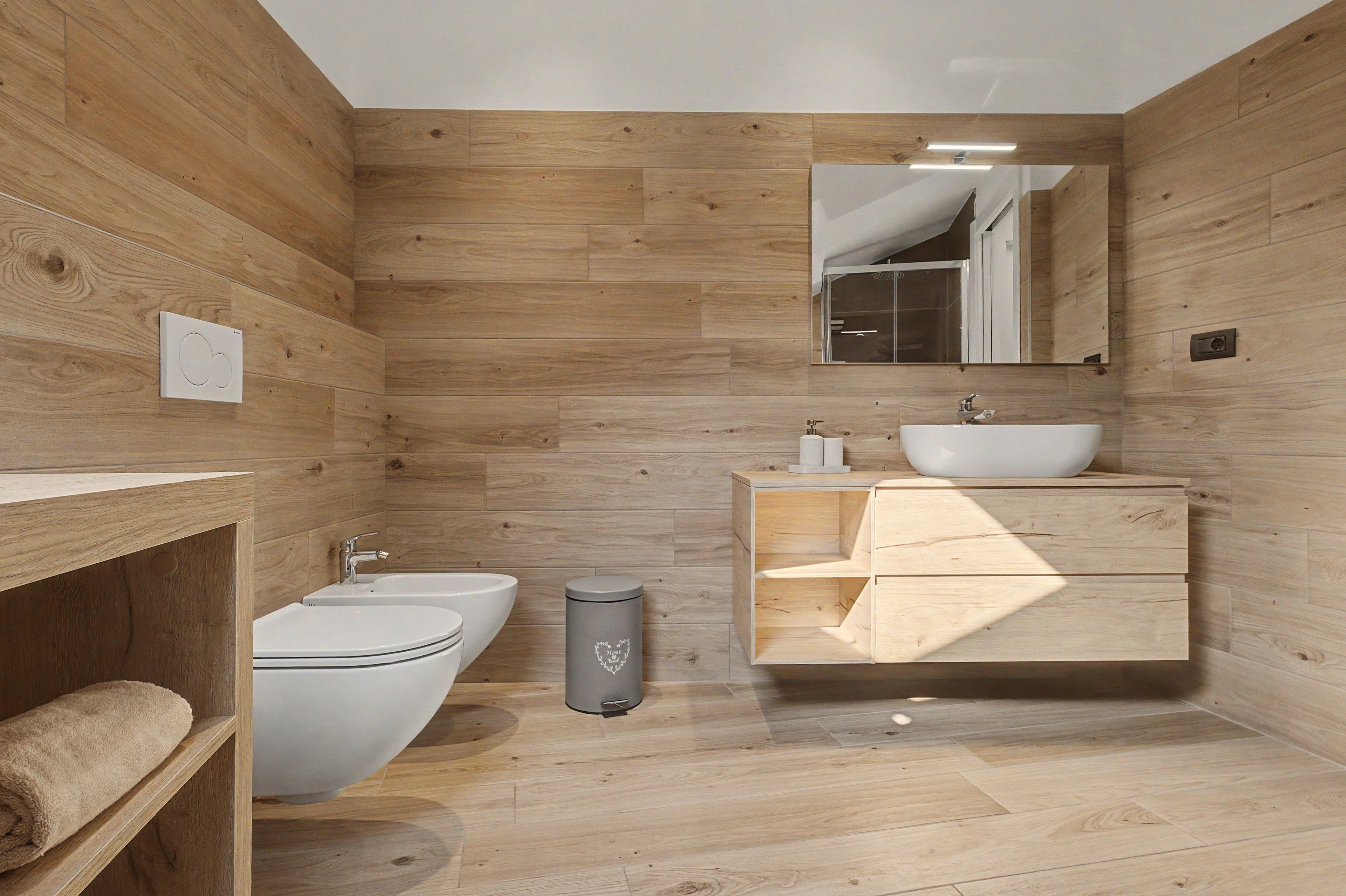Une salle de bain moderne avec des murs recouverts de panneaux en bois, un lavabo blanc, des toilettes et un bidet.