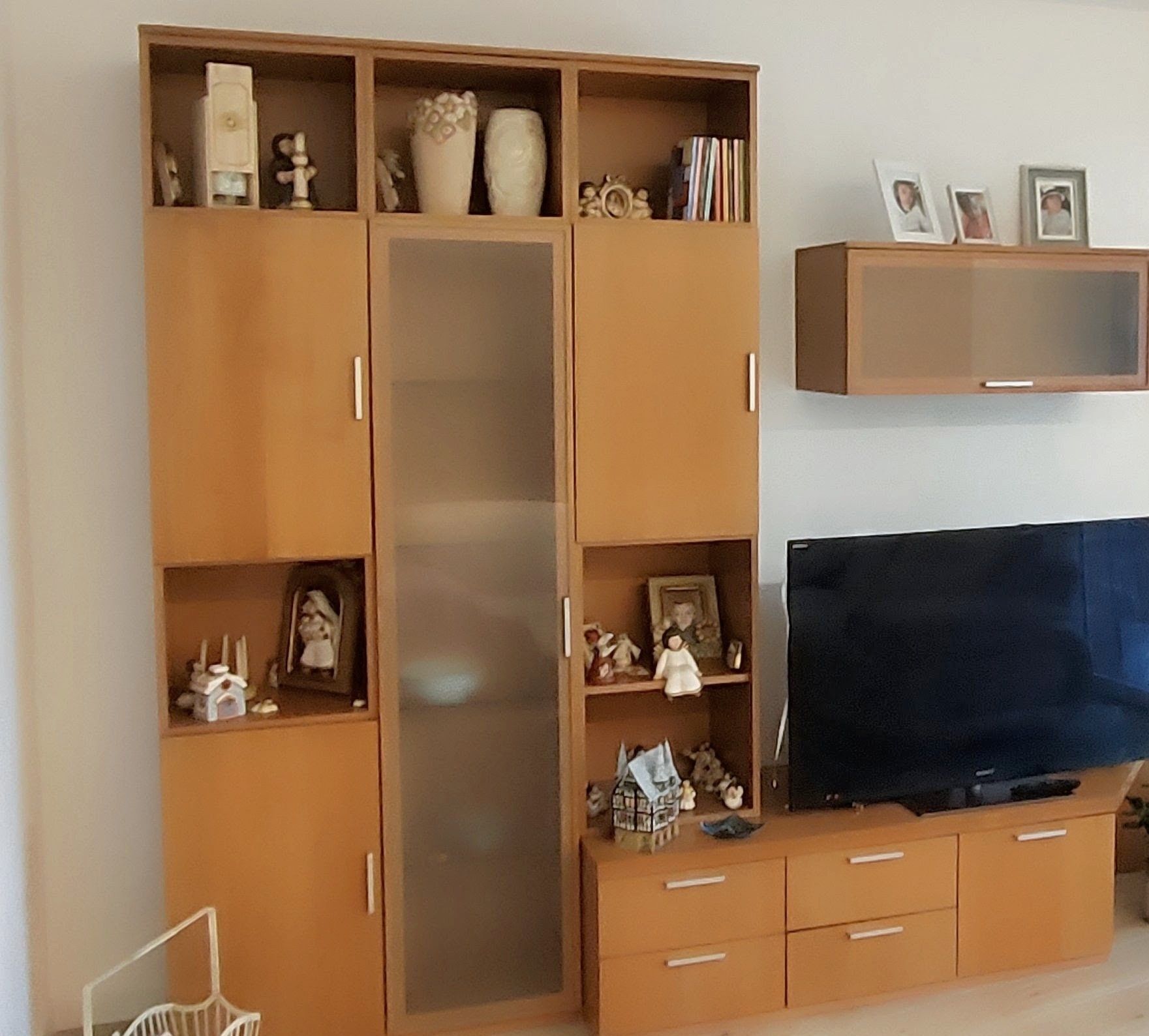 Una sala de estar con un televisor grande, armarios de madera y estantes con diversos objetos.