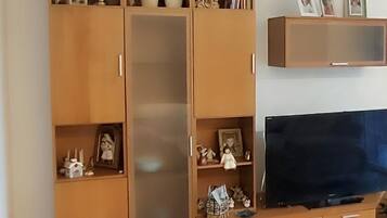 Una sala de estar con un televisor grande, armarios de madera y estantes con diversos objetos.