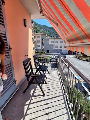 Ein Balkon mit Stühlen und einem Tisch, der auf eine Straße und Gebäude blickt.