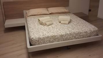 Een moderne slaapkamer met een houten vloer, een bed met een bedovertrek met een patroon, twee kussens en twee opgerolde handdoeken.