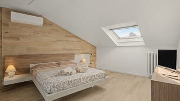 Ein Schlafzimmer mit schrägverdeckter Decke, einem Bett mit Kopfteil, einem Nachttisch mit Lampe, einem Heizkörper und einem Fernseher.