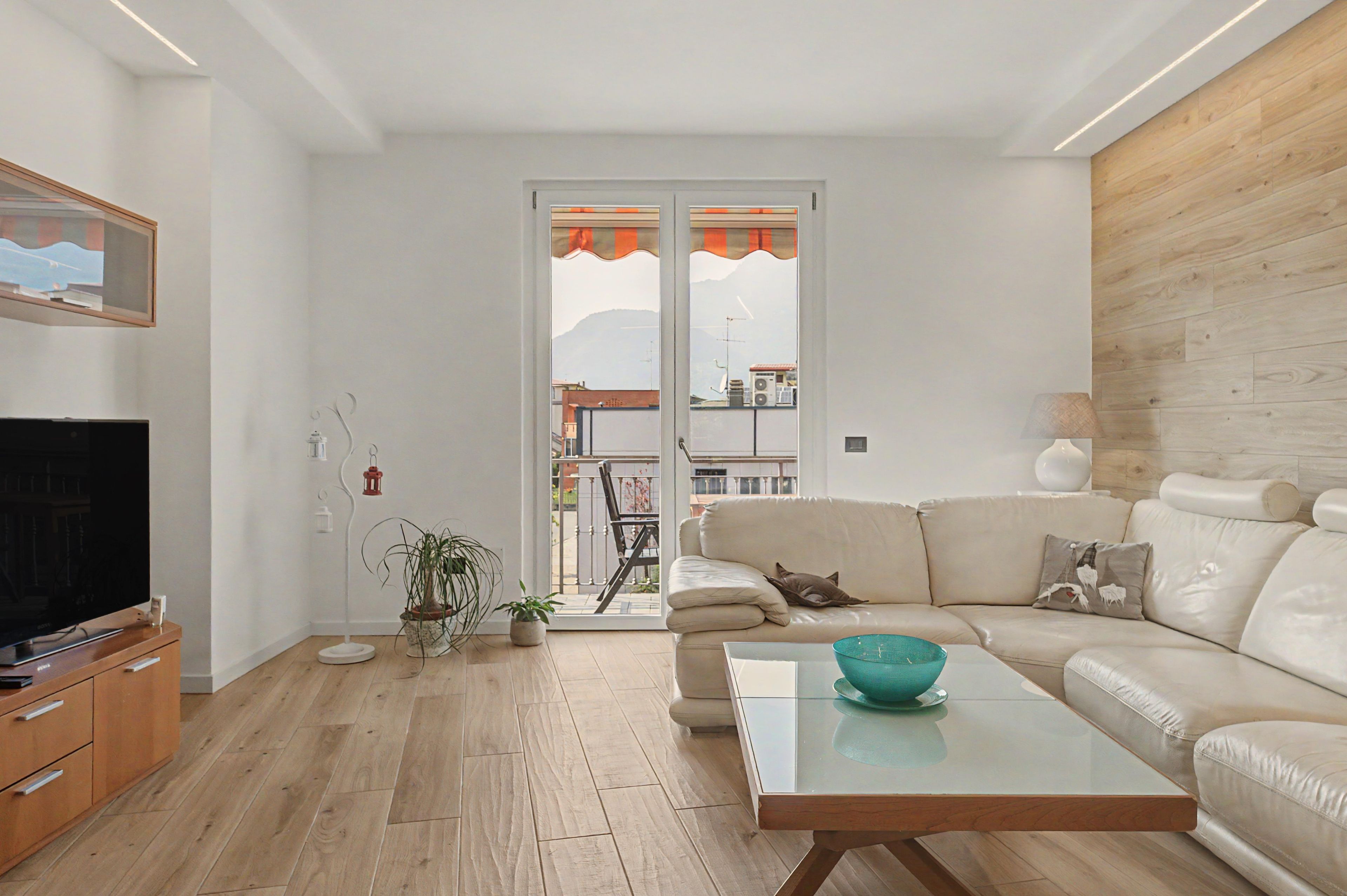 Una sala de estar moderna con un televisor de pantalla plana, piso de madera, un sofá, una mesa de centro y un balcón con vistas.