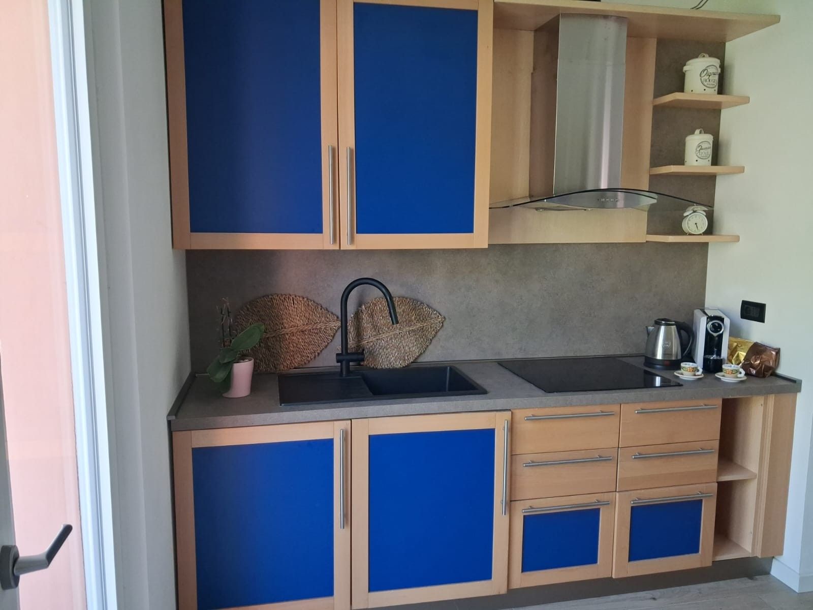 Une cuisine compacte avec des meubles de rangement bleus, un évier, une bouilloire et une machine à café.