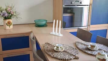Una cucina moderna con forno a incasso, un tavolo da pranzo con sottopiatti e un vaso decorativo con fiori.