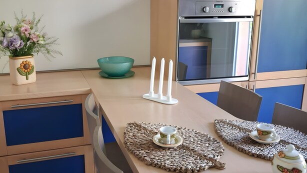 A modern kitchen with a built-in oven, a dining table with placemats, and a decorative vase with flowers. - Apartment 'Eddy Home' with Wi-Fi (Bellano)
