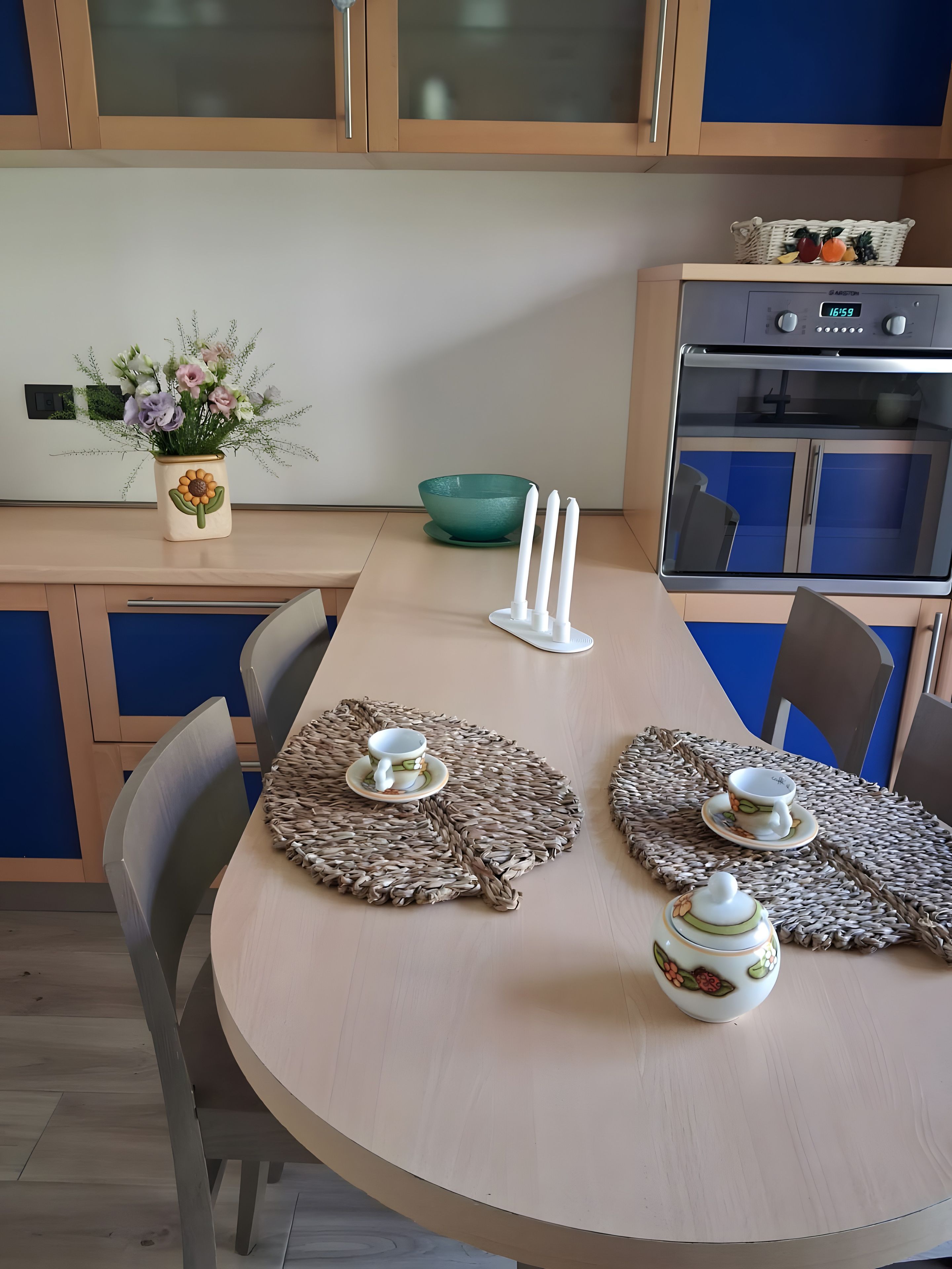 A modern kitchen with a dining table set for two, featuring a woven placemat, a teapot, and a cup.