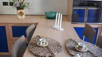 A modern kitchen with a dining table set for two, featuring a woven placemat, a teapot, and a cup.