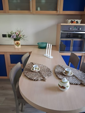 Una cocina moderna con una mesa de comedor preparada para dos personas, que incluye un mantel tejido, un juego de té y una taza.