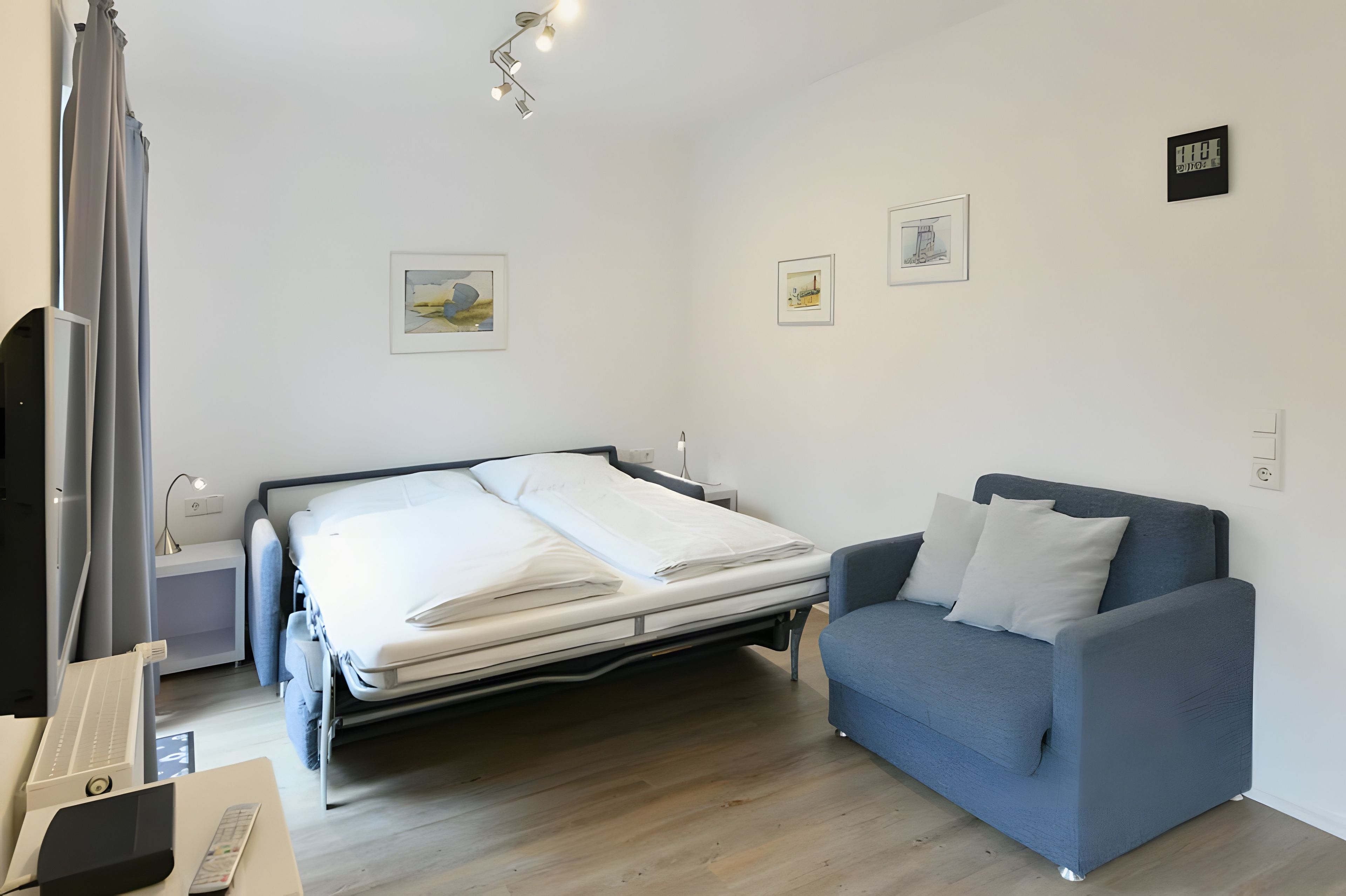 Une chambre d’hôtel avec un lit, un canapé bleu, un bureau avec une lampe et des œuvres d’art accrochées aux murs.