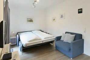 Habitación de hotel con cama, sofá azul, escritorio con lámpara y obras de arte en las paredes.