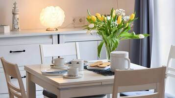A dining area with a table set for two, a vase of flowers, and a lit lamp.