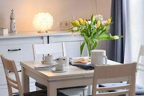 Un área de comedor con una mesa preparada para dos, un jarrón de flores y una lámpara encendida.