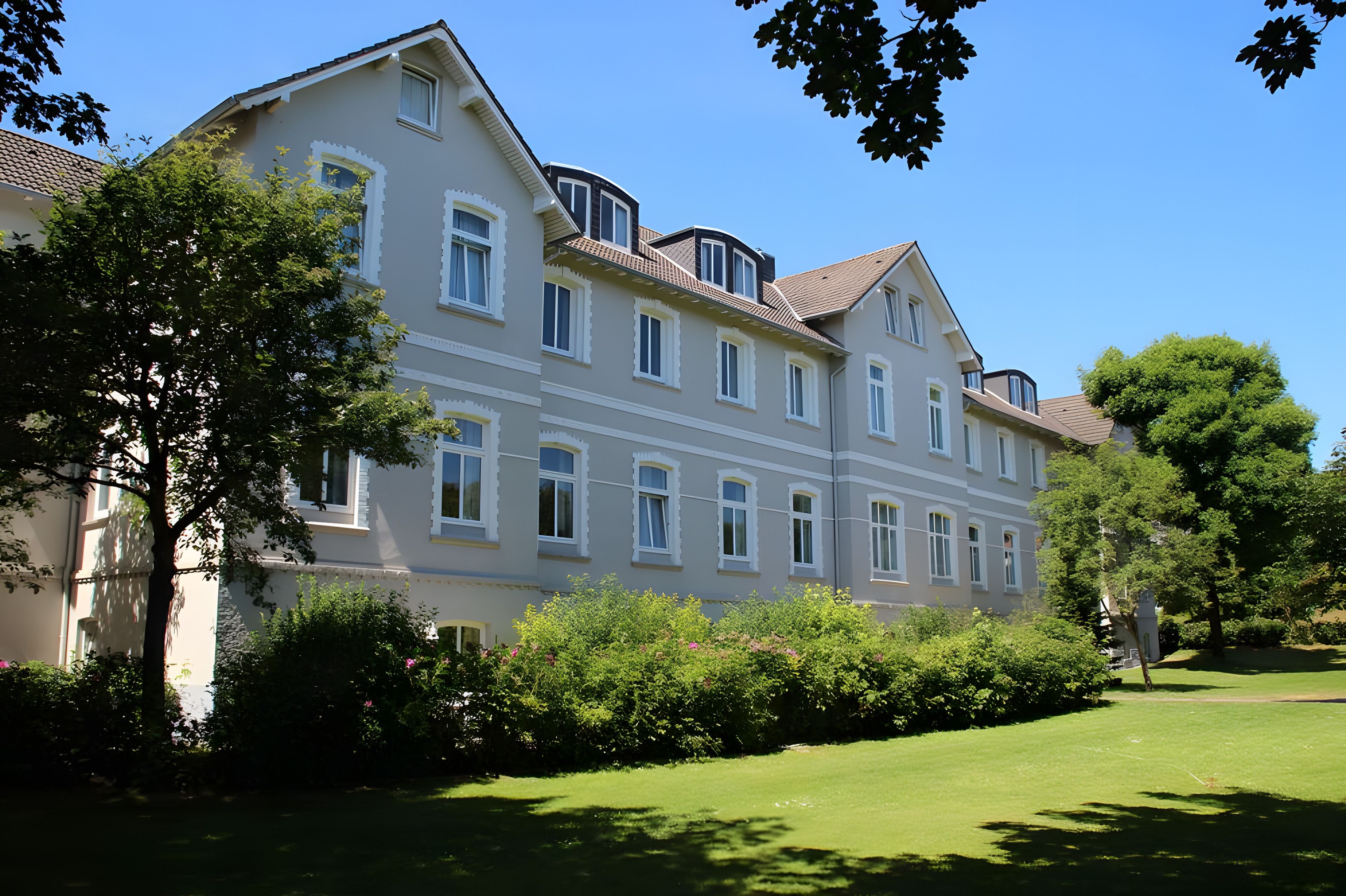 Ein mehrgeschossiges Gebäude mit einer symmetrischen Fassade, großen Fenstern und einem gepflegten Rasen.