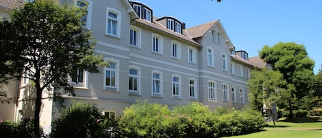 Un edificio de varios pisos con fachada simétrica, amplias ventanas y césped cuidado.