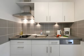 A modern kitchen with white cabinets, a stainless steel range hood, a built-in dishwasher, and a coffee maker. - Comfortable, Modern Apartment in a Central, Quiet Island Location for 2 Guests (Wangerooge)