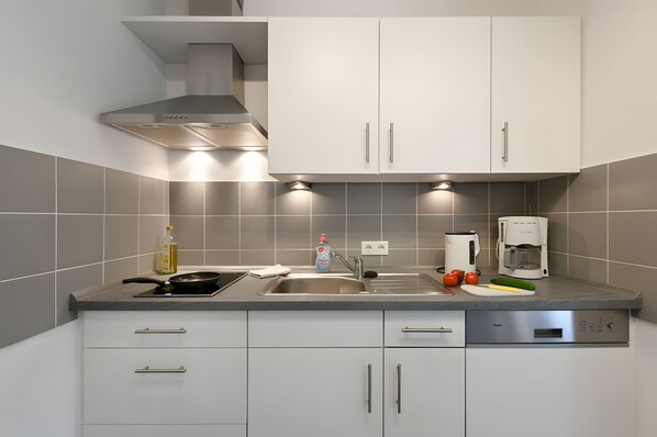 Una cocina moderna con armarios blancos, una campana extractora de acero inoxidable, lavavajillas integrado y una cafetera.