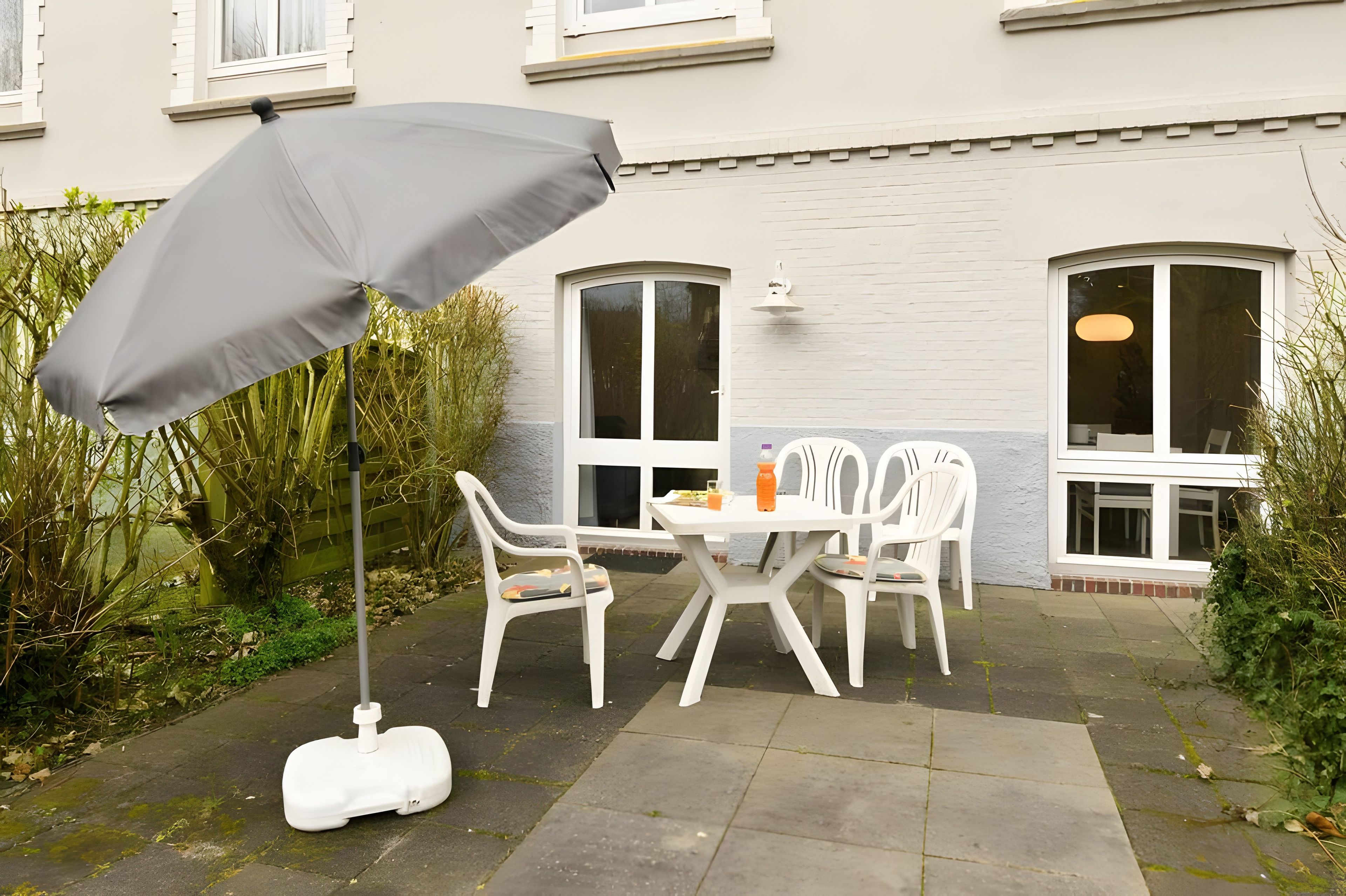 Eine Terrasse im Freien mit Tisch und Stühlen, einem grauen Sonnenschirm und einem weißen Rasenmäher.