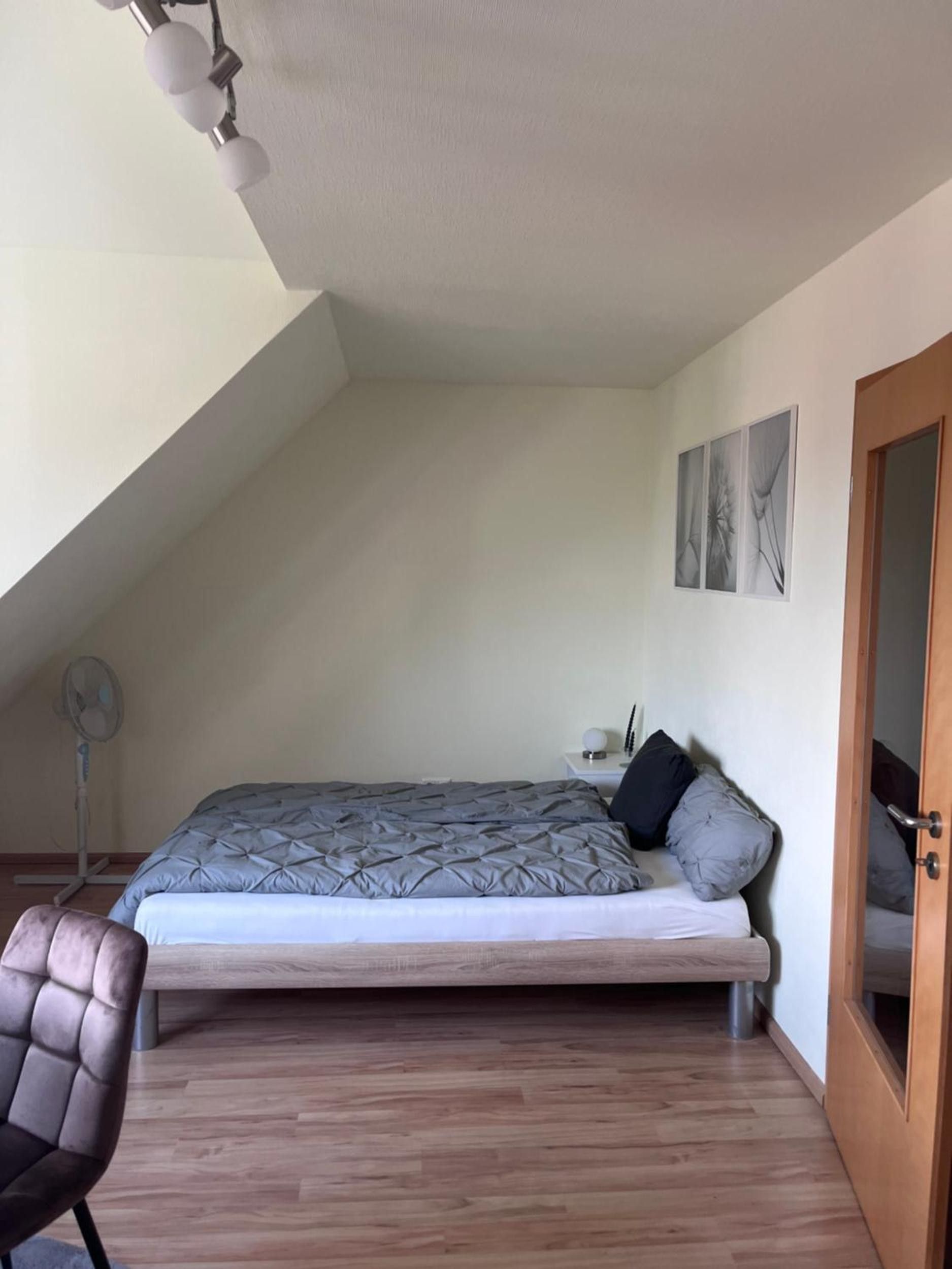 Ein Schlafzimmer mit einem Bett, einem Sessel, einem Ventilator und einer Tür.