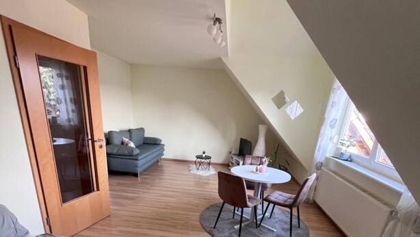 Quarto com cama, mesa redonda pequena com cadeiras, sofá e porta que dá para outro cômodo.