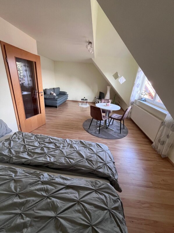 Ein Schlafzimmer mit einem Bett, einem kleinen runden Tisch mit Stühlen, einem Sofa und einer Tür zu einem anderen Raum.