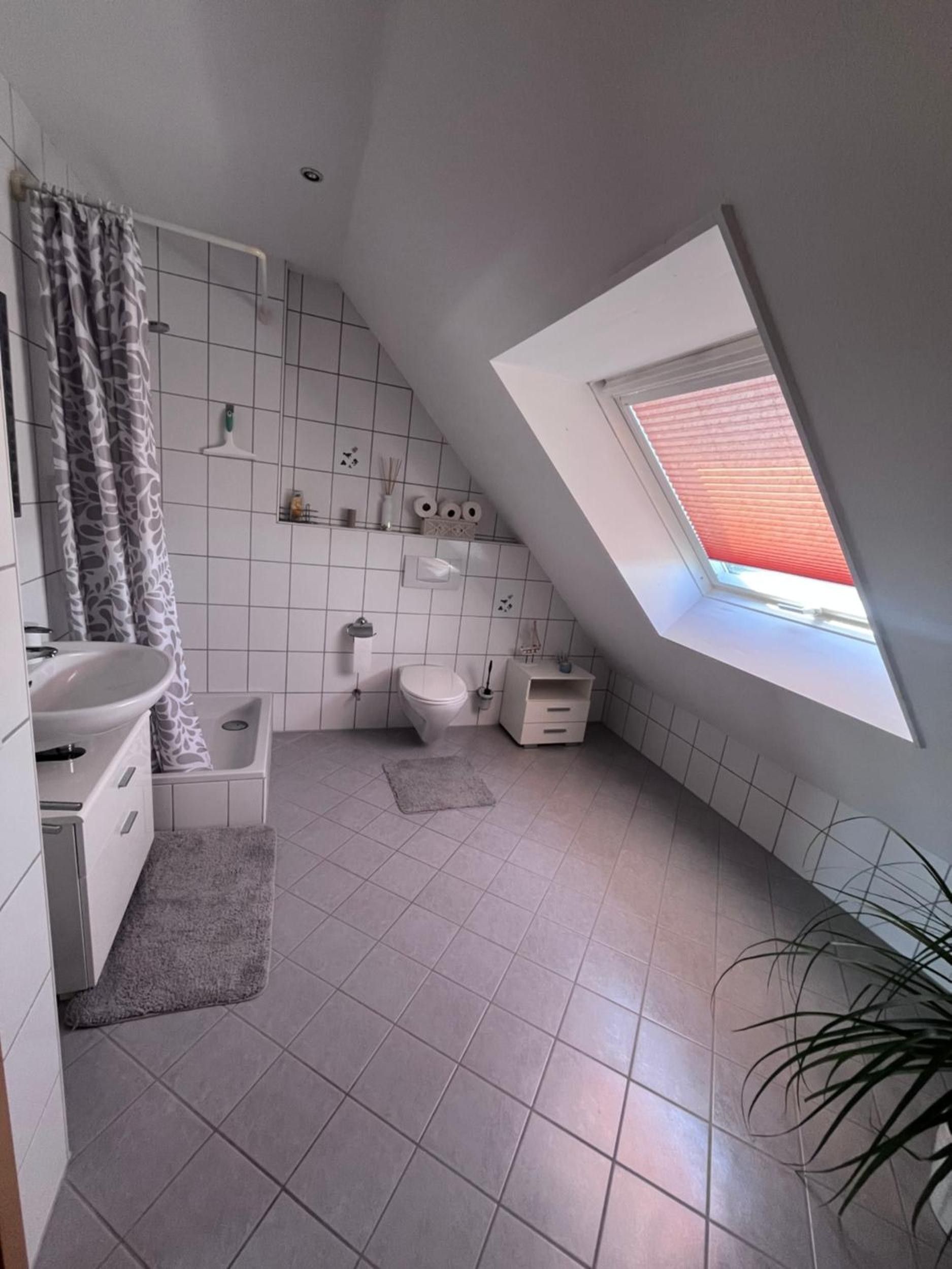 Ein modernes Badezimmer mit Oberlicht, weißen Fliesen, einer Dusche, einer Toilette und einem Waschbecken.