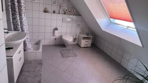 Casa de banho moderna com claraboia, azulejos brancos, chuveiro, sanita e lavatório.