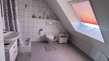 Ein modernes Badezimmer mit Oberlicht, weißen Fliesen, einer Dusche, einer Toilette und einem Waschbecken.