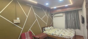 Une chambre avec un lit, une chaise, un mur orné de motifs géométriques, un climatiseur et une prise de courant.