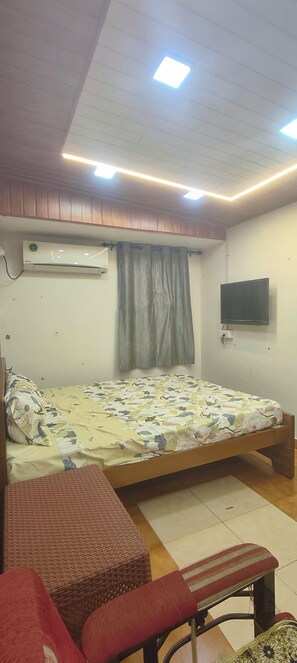 Een slaapkamer met een bed, een televisie, een airconditioner en een raam met gordijnen.