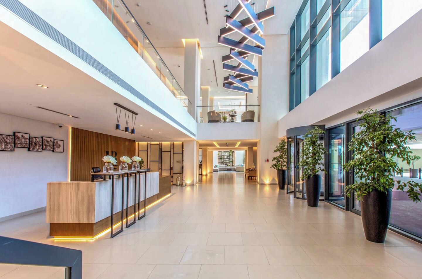 A spacious lobby with a reception desk, large potted plants, and a modern ceiling design.