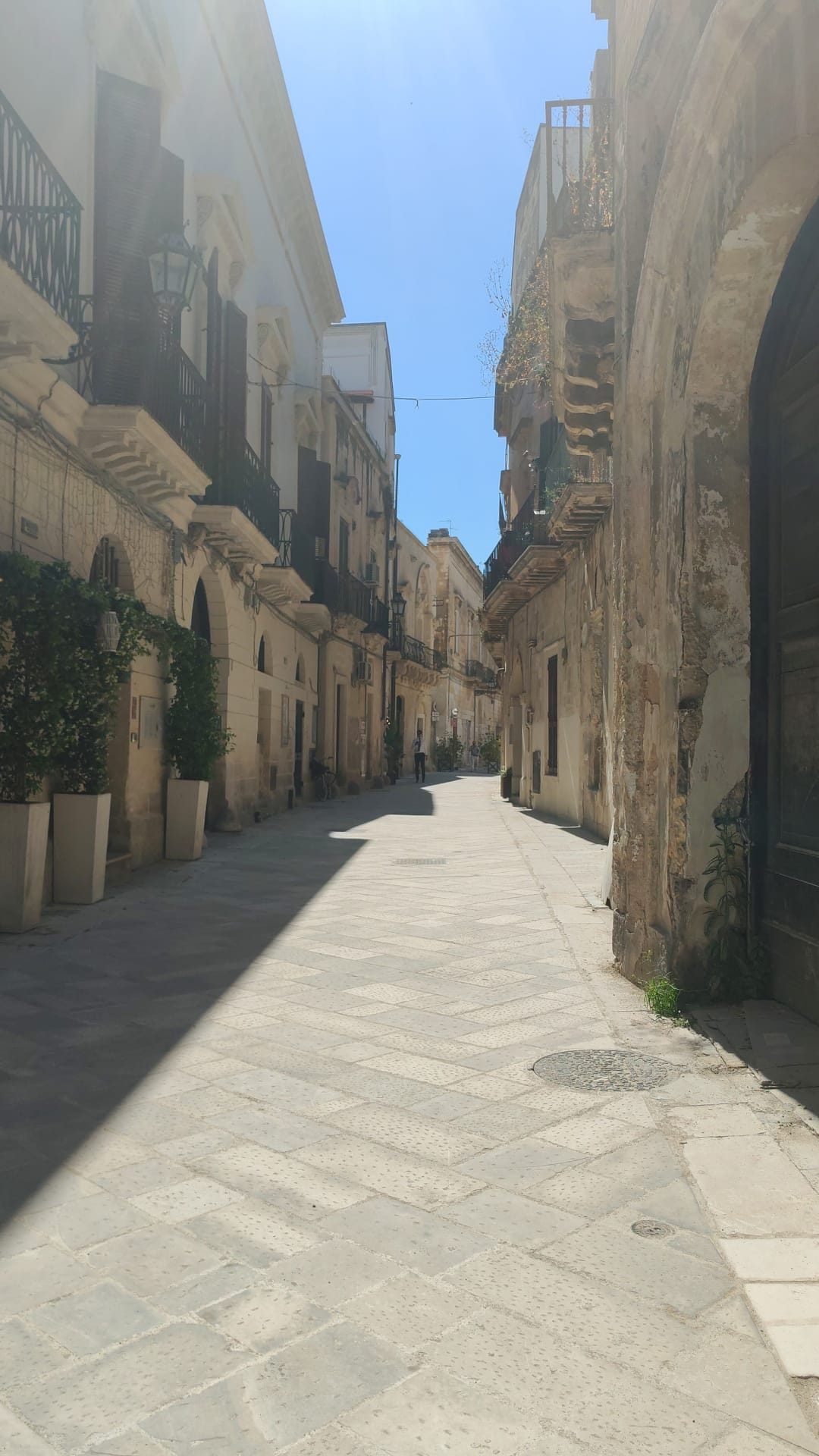 A narrow street with historic buildings, a paved walkway, and a clear sky.