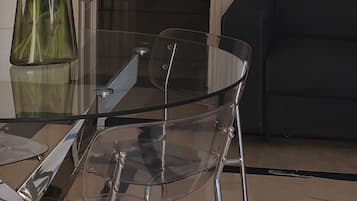 A dining area with a glass table and chairs, a vase with flowers, and a black sofa in the background.