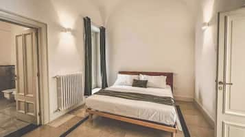 A bedroom with a bed, a radiator, a door, and a mirror.
