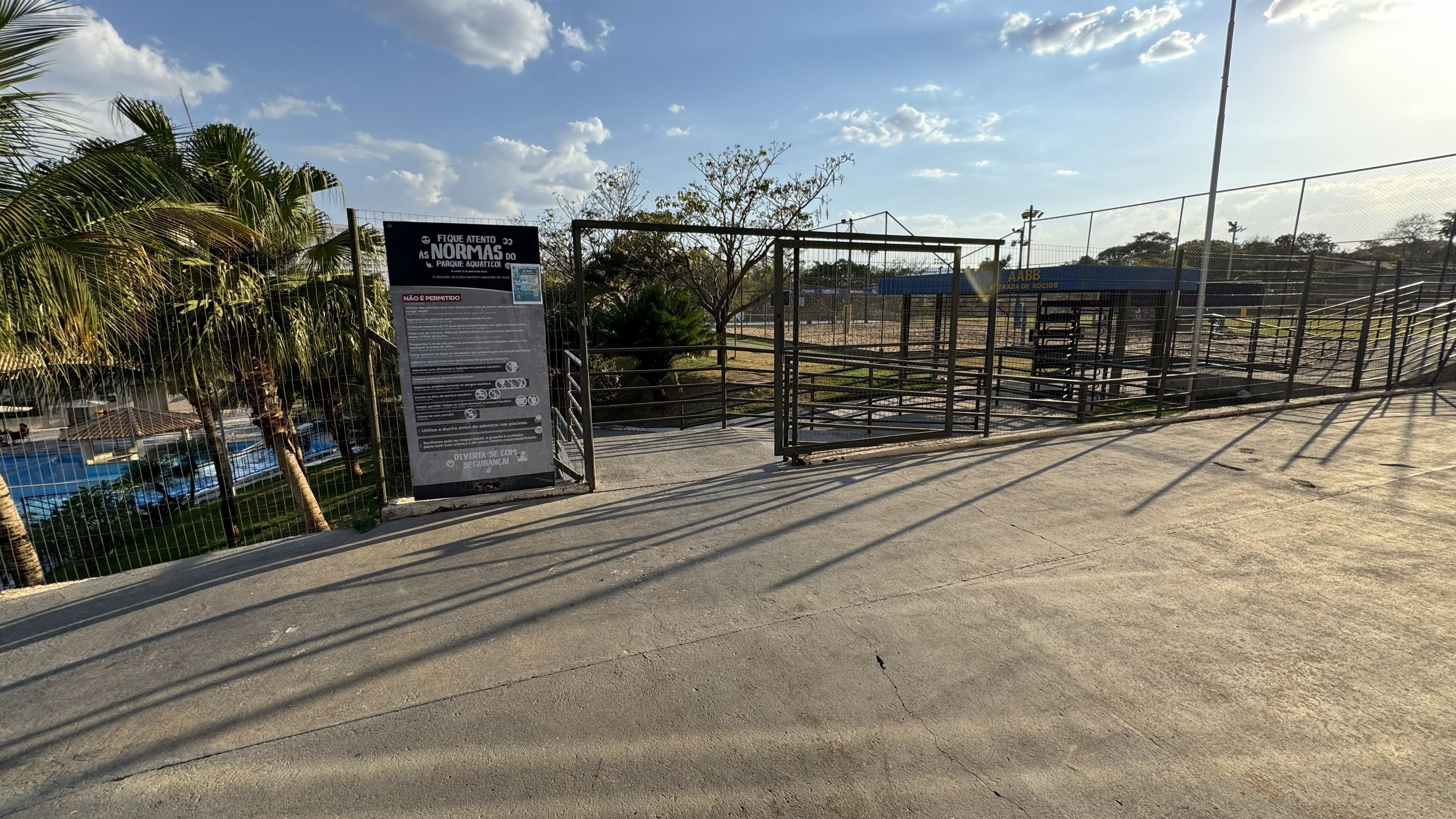 Zona vallada con un cartel, un camino de hormigón y una piscina al fondo.