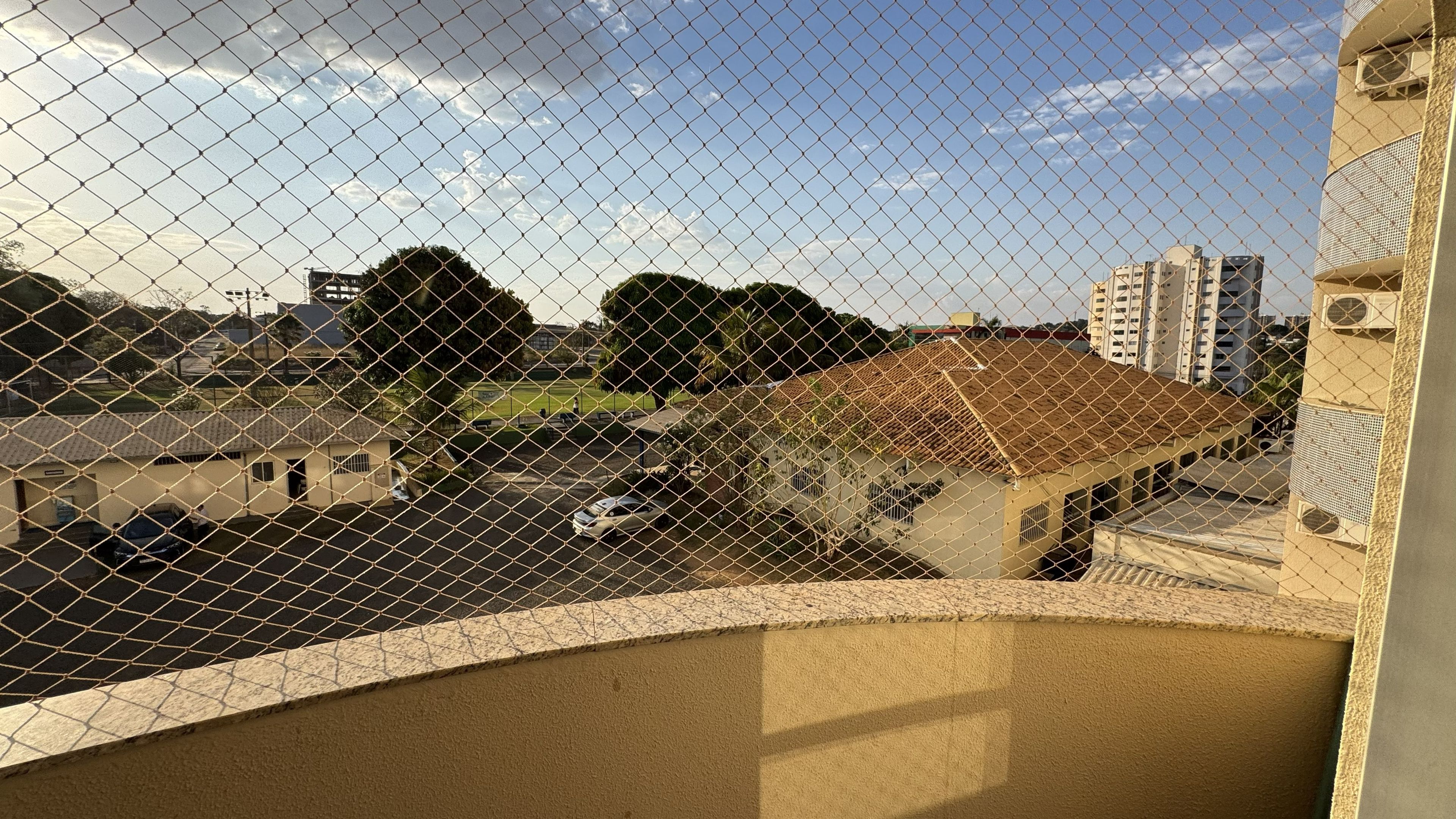 A chain-link fence with a view of a building with a tiled roof and a flat roof structure in the background.