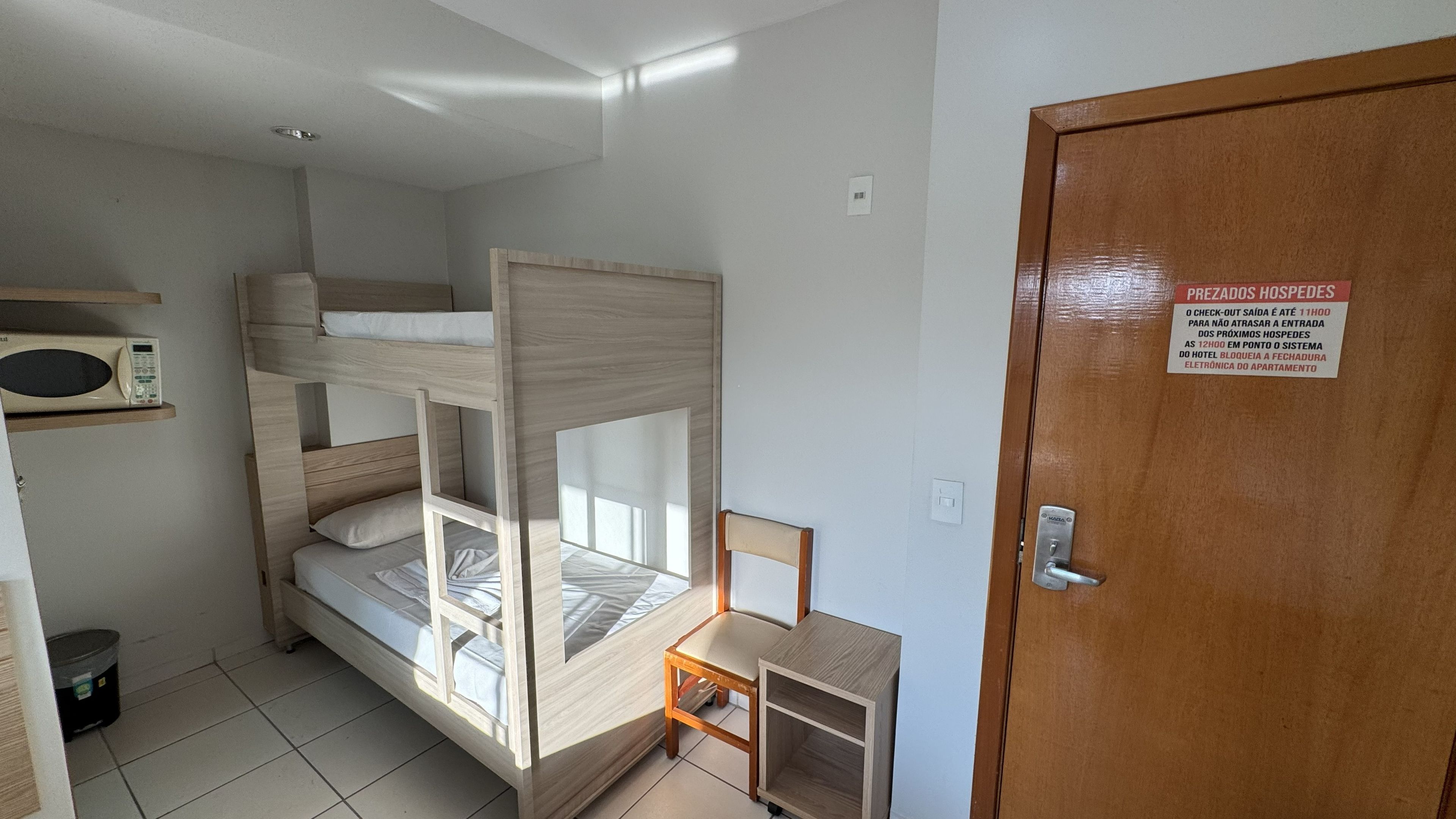 A room with bunk beds, a microwave, a small table, and a door with a sign.