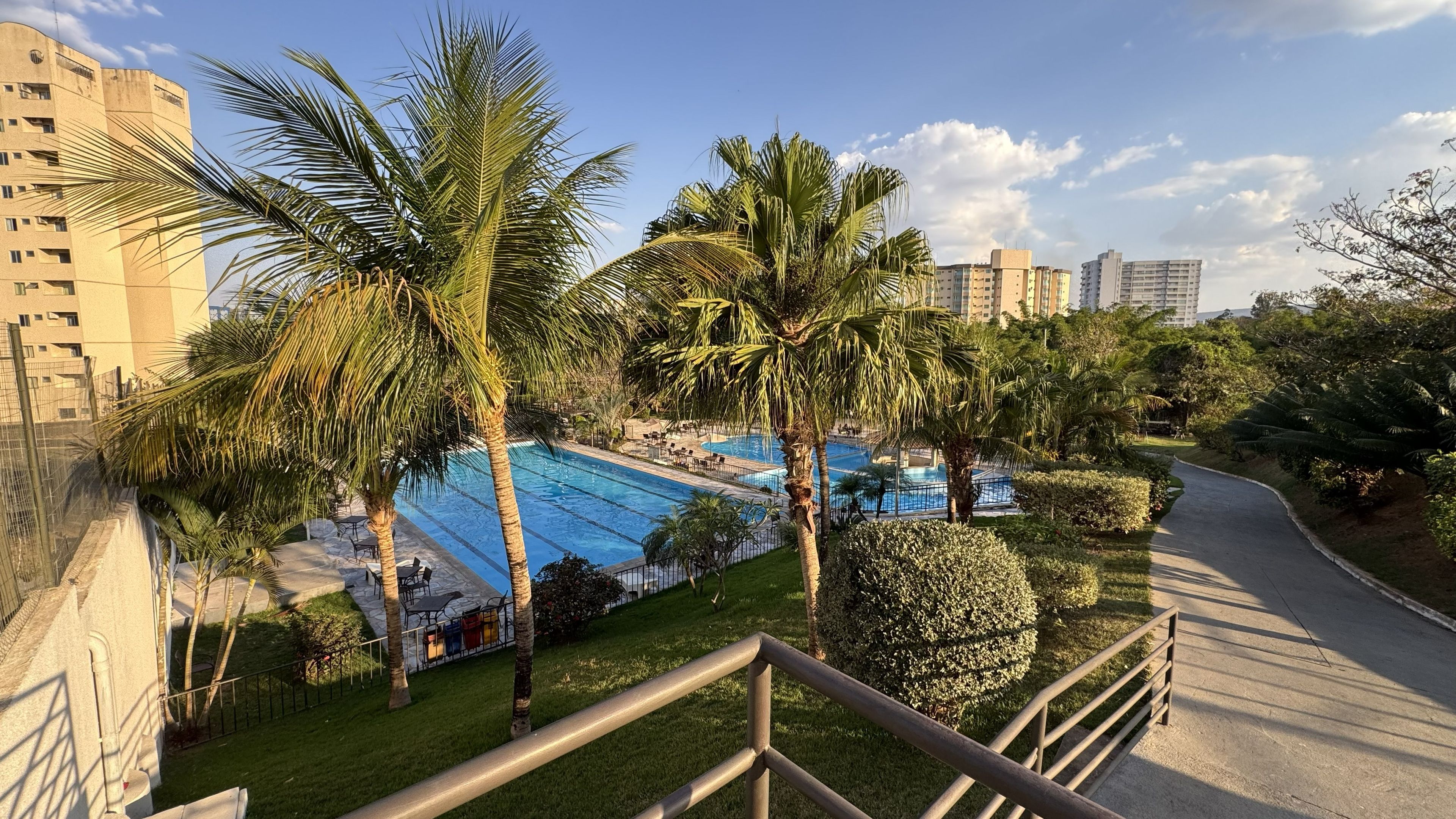 Área residencial com piscina, palmeiras e um calçadão.