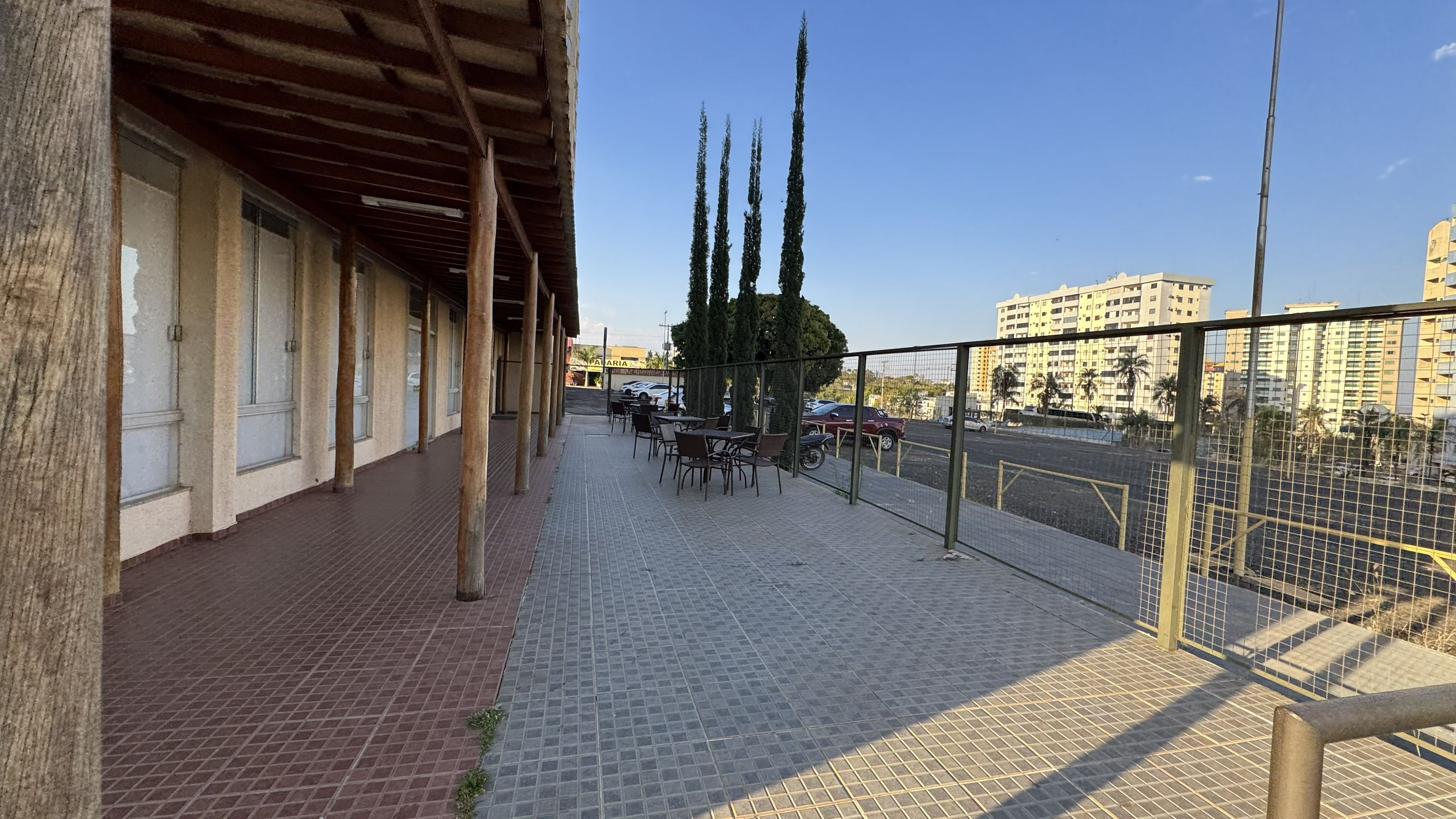 A covered outdoor seating area with tables and chairs, a tiled floor, and a view of a cityscape with buildings and a road.