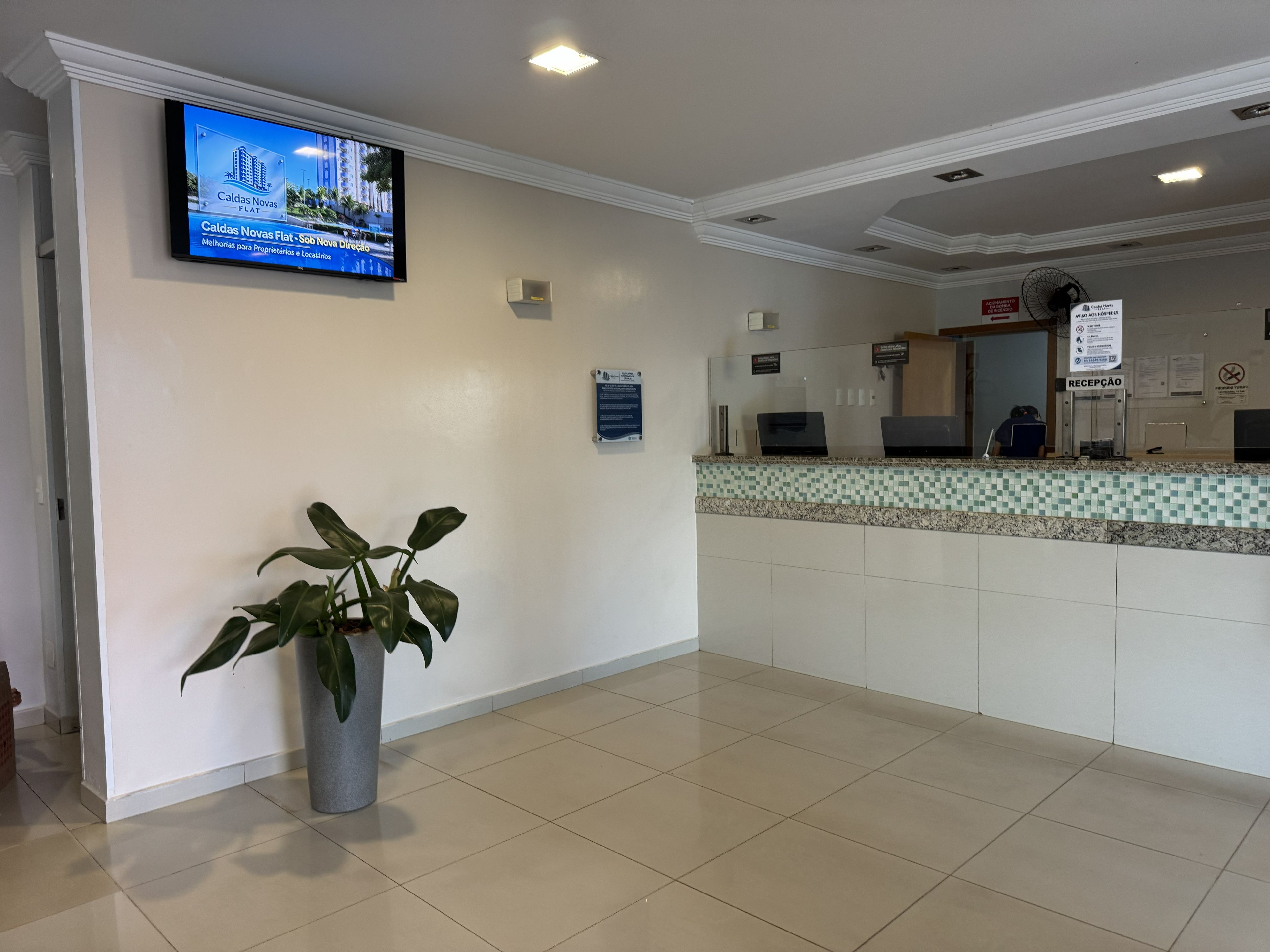A reception area with a flat-screen TV displaying a property, a reception desk, and a potted plant.