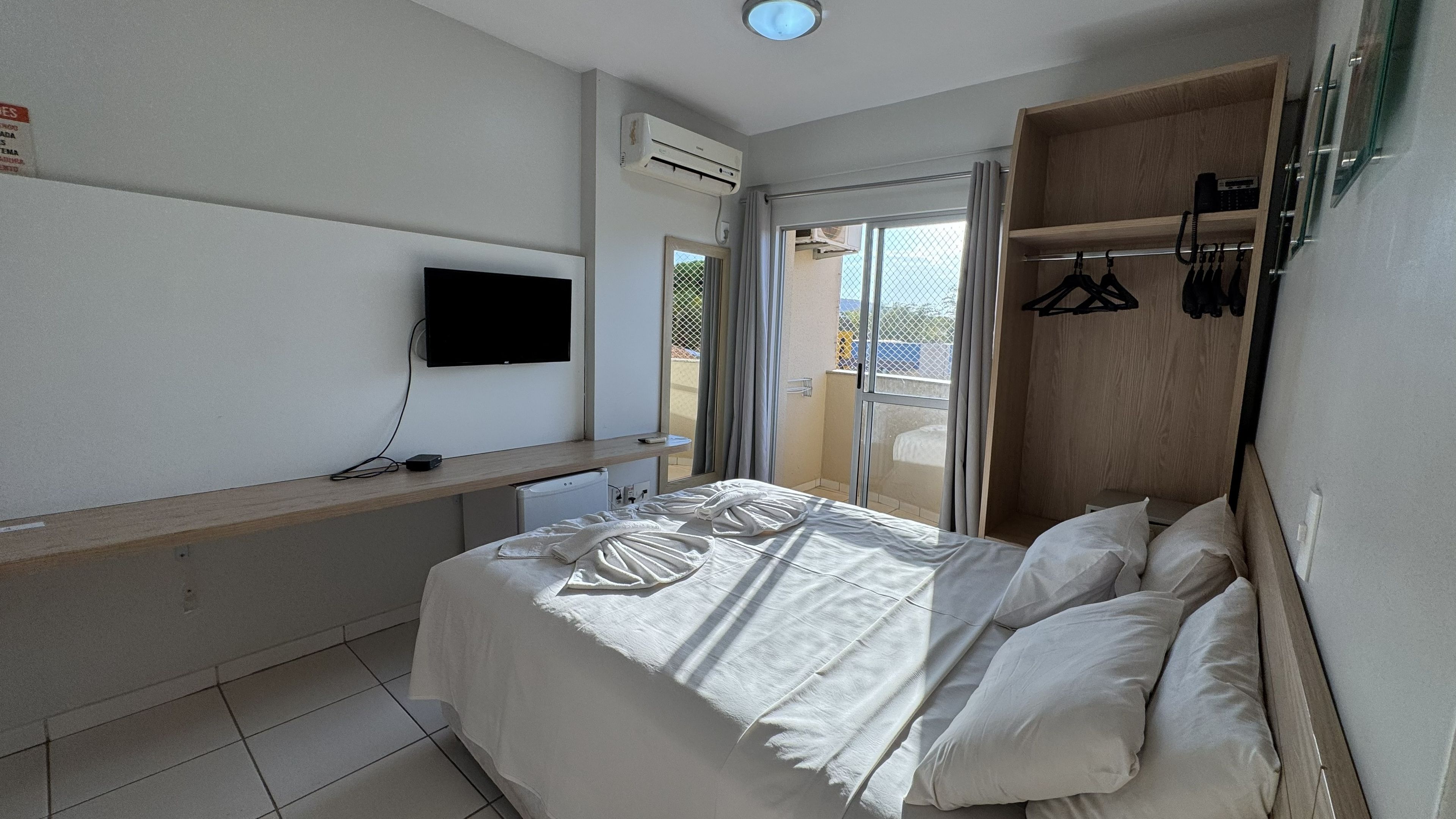 Ein Hotelzimmer mit einem Bett, einem Flachbildfernseher, einem Holztisch und einem Kleiderschrank.
