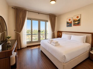 A hotel room with a large bed, a desk, a mirror, and a view of the outdoors. - Vesta Luxury APT - 2Br - cfc xc (New Cairo)