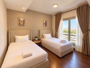 A hotel room with two beds, a small table, a potted plant, and a view of the city. - Vesta Luxury APT - 2Br - cfc xc (New Cairo)