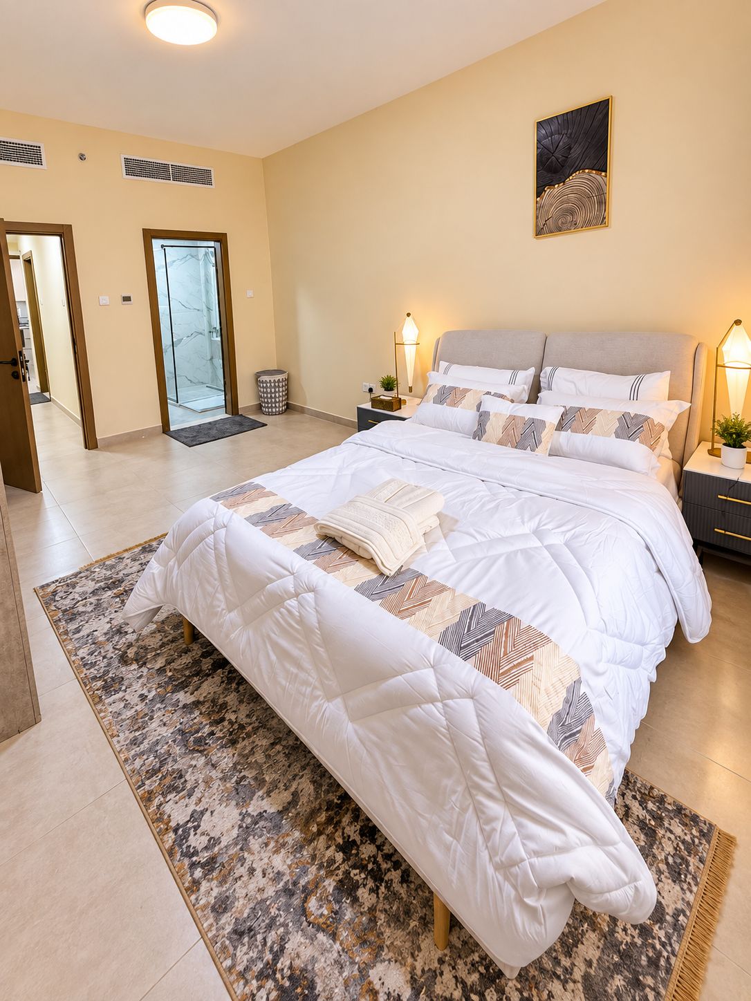 Una camera da letto moderna con un letto grande, comodini, uno scaffale e un’opera d’arte a parete, oltre a un bagno con doccia in vetro.