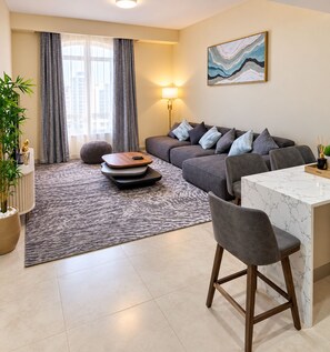 Un salon moderne avec un canapé gris, une table basse, un coin repas avec une table en marbre et une grande fenêtre avec des rideaux.