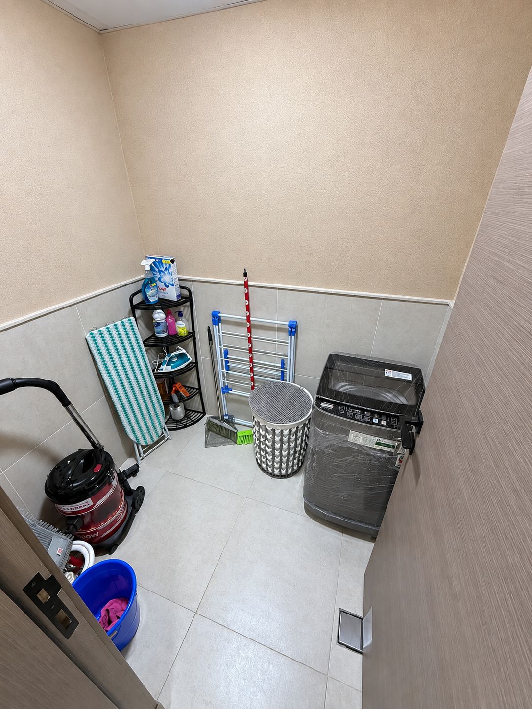 Une petite pièce propre, équipée d’un aspirateur, d’une poubelle, d’un panier à linge et d’une étagère contenant des produits de nettoyage.