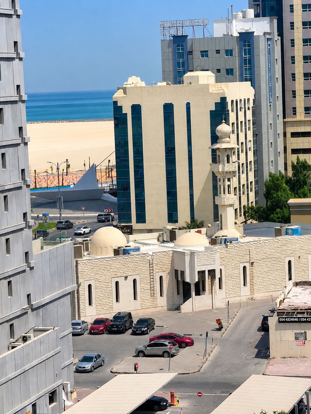 Un hôtel au design moderne, doté d'une enseigne bien visible, offrant une vue sur la plage et disposant d'un parking pouvant accueillir plusieurs voitures.