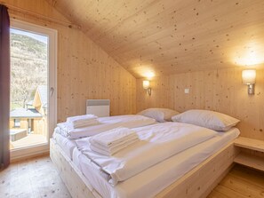 A wooden cabin room with two beds, a heater, and a window with a view of a building and trees. - One-bedroom Cabin (Sankt Georgen am Kreischberg)